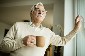 Pensive mature man with cup of coffee looking through the window.