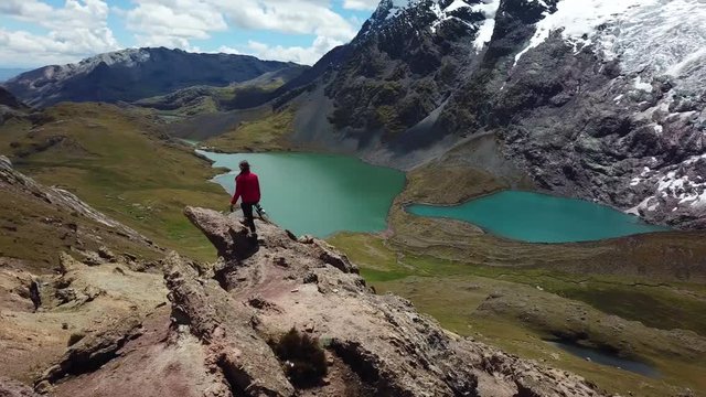 Aerial, drone shot around a womanwalking to the top of a cliff, in front of the Ausangate Glacier mountain, on a sunny day, in the Andes, Peru, South America