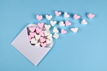 Pink and white heart shaped marshmallow hearts spilling out of white love letter envelope on light blue background