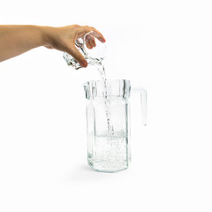Hand pours water from a glass cup into a jug, isolated on white background