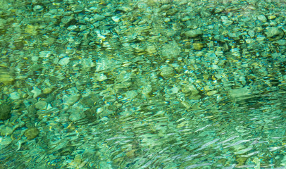 Fototapeta na wymiar Abstract background with crystal clear emerald ripply water surface and pebble under water, Verzasca river, Switzerland