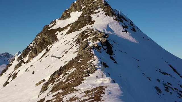 Drone shot, flying up a snow covered mountain ridge to the top peak which then reveals a mountain landscape including Mont Blanc, in La Plagne France