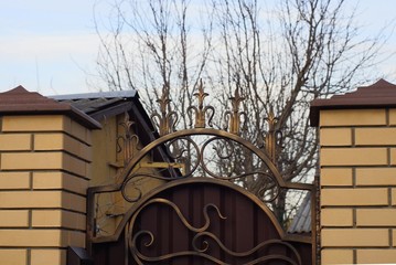 part of a brown brick fence and part of an iron gate with a forged pattern and sharp rods against...