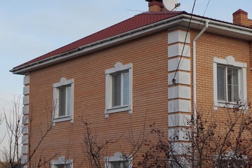 large private brown brick house with white windows under a red tiled roof against a blue sky