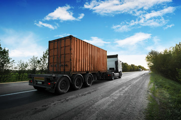 Truck with a container on a countryside road against a sky with clouds