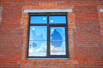 a broken new window on the wall of a red house that reflects the clouds and sky