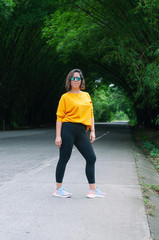 Woman in yellow sweater and sunglasses, with winning attitude, stop on natural bamboo road, during spring break trip