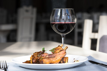 Ribs in honey onion glaze on a white plate with a glass of red wine