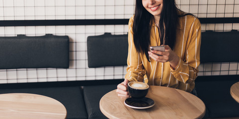 Young woman with cup of coffee talking with friend by smart phone in city cafe