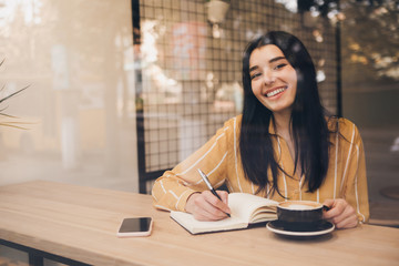 Pretty woman in urban cafe write book with laptop and black coffee