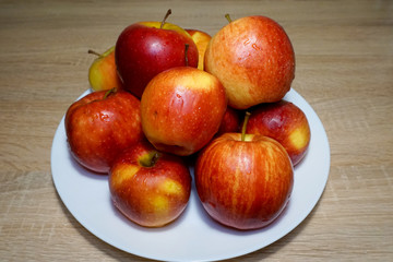 Ripe bright red Florina apples on a white ceramic plate on a wooden table