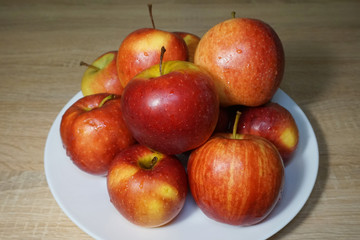 Ripe bright red Florina apples on a white ceramic plate on a wooden table