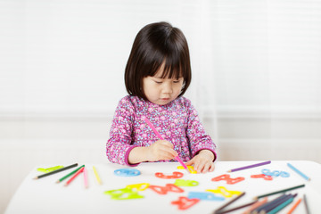 toddler girl practice writing letters on white paper against white background