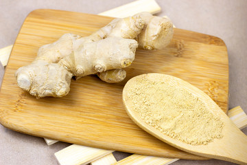 Fresh raw yellow ginger root with ground dry powder in wooden spoon and on wood background.