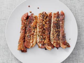 Raw uncooked pork belly slices marinated with Asian style soy souse and herbs on a white plate on simple table cloth.