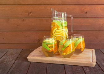 White wine sangria with fruits in glasses and pitcher on cutting board on aged wooden table.