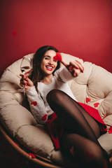 Laughing lovable woman with wineglass having fun in studio. Carefree female model in black pantyhose posing with paper heart.