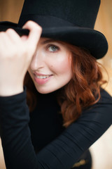 Portrait of a red-haired girl smiling in a black top hat and body suit. On a gold background. Cabaret dancer. Art deco style 20 years.