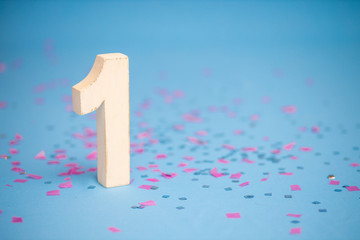 White wooden unit on a background of confetti and sparkles. First birthday.