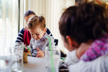 Obraz premium Small little boy caucasian child son sitting in the lap of his mother or aunt while female friend is looking at them teasing smiling holding smart mobile phone playing games making video call family