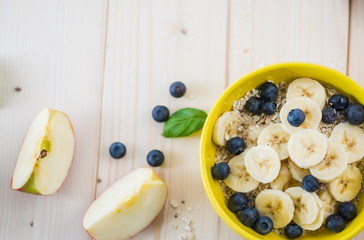 Morning breakfast with fruit pieces and blueberries all on a light wooden table.