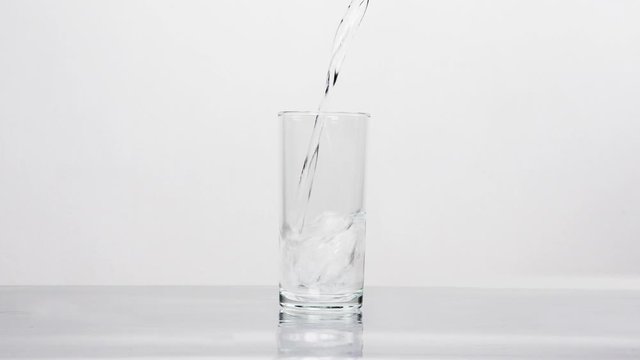 Smooth water pouring into transparent glass on the table. White background
