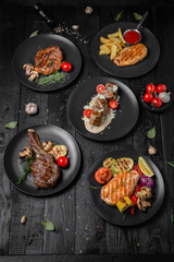 Plates with dishes: beef steak on a bone, grilled salmon fillet, skewers in a creamy sauce, pork steak, grilled chicken fillet with sauce. Octoberfest party dinner. Festive table with delicious food