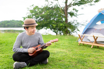 Naklejka na ściany i meble smart asian man sitting on green grass and playing ukulele, he relax and feeling happy, he training to artist