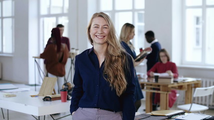 Medium shot portrait of happy positive young blonde business woman smiling at camera at modern loft office workplace.