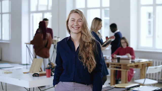 Medium Shot Portrait Of Happy Positive Young Blonde Business Woman Smiling At Camera At Modern Loft Office Workplace.