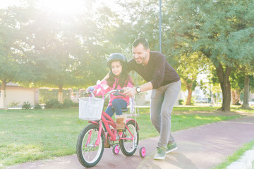 Happy Daughter Learning To Ride Bicycle From Father