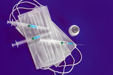 Surgical or viral mask, syringes and vaccine ampoule on a blue background. Virus epidemic concept, medical concept.
