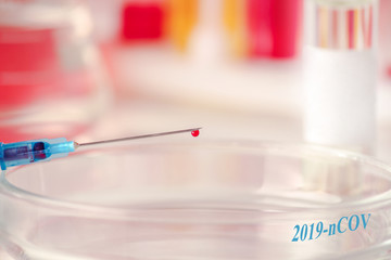 Syringe with a blood sample on the background of medical ampoules and laboratory glassware. Virus epidemic, medical concept with the inscription - 2019-nCOV.