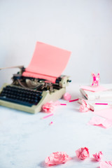 Pink crumpled paper balls and a typewriter on a writer workplace. Feminine creative occupation.