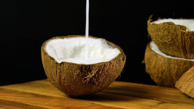 Healthy nutritious natural coconut with a vast range of dietary and cosmetic advantages and uses, show here pouring coconut milk into a half shell on wooden chopping board against a black background.