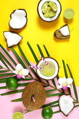 Fototapeta na wymiar Coconut summertime entertaining theme flat lay creative layout overhead with coconuts filled with summer drinks and cocktails on modern pink and yellow table top.