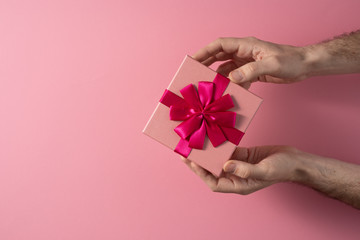 Valentine's Day celebration concept. A nice gift from a loved one. Box with a bow in male hands on a delicate pink background. Copy space. Flat lay.