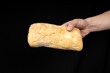 Fresh bread ciabatta in the male hand on black background.
