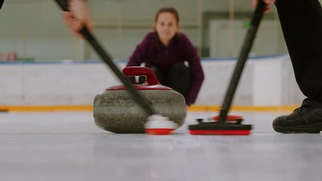 Curling training - rubbing the ice before the biter with red handle - third woman watching other players