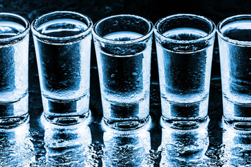 Vodka shots in a row. Neon blue bar encounter. Wet glass transparent liquor. Dark black addiction...