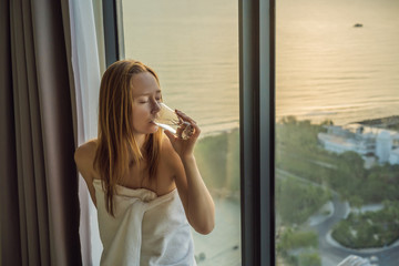 Woman drinks water in the morning on a background of a window with a sea view