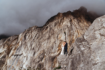 Young newly wed couple, bride and groom kissing, hugging on perfect view of mountains, wedding concept