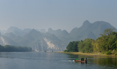 Old barge and cruise boats on the Li River Guangxi China with karst dome mountains