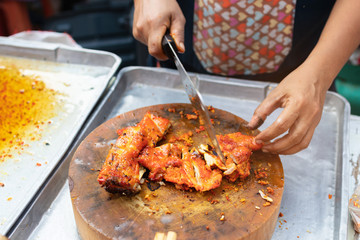 Street vendor cutting a grilled chicken marinated with curcuma on wooden cutting board; Thai street food market. 