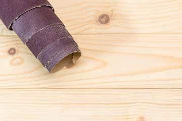 sandpaper twisted into a roll lies on a wooden board. Close-up. There is a tint.