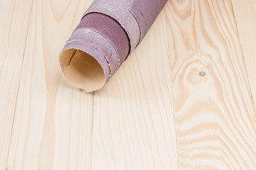 sandpaper twisted into a roll lies on a wooden board. Close-up. There is a tint.