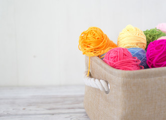 Bright colored threads for knitting in a basket on a wooden background