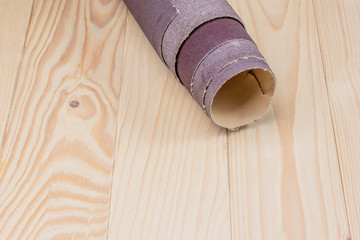 sandpaper twisted into a roll lies on a wooden board. Close-up. There is a tint.