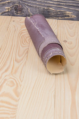 sandpaper twisted into a roll lies on a wooden board. Close-up. There is a tint.