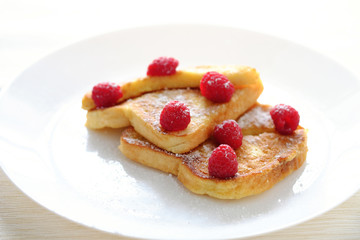 Two sweet toasts with raspberries sprinkled with sugar served on a white plate.